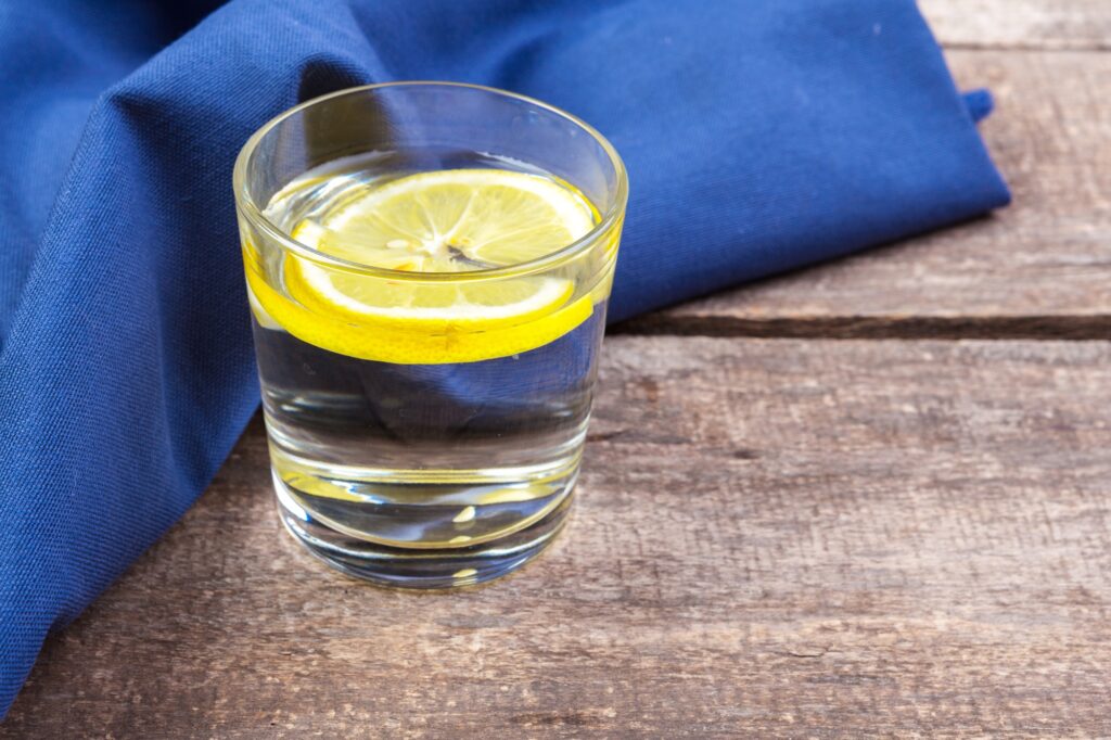 Glass with water and lemon on wooden table jajandikitid Mengatasi Bau Mulut dengan Air Lemon