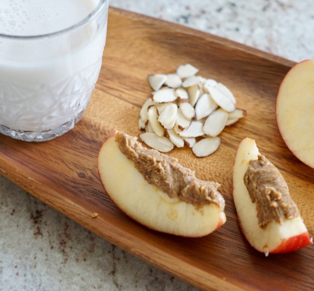 Slivered almonds almond butter on apple slices and almond milk on a wooden tray jajandikitid apel dan selai almond makan sehat sebelum jalan pagi