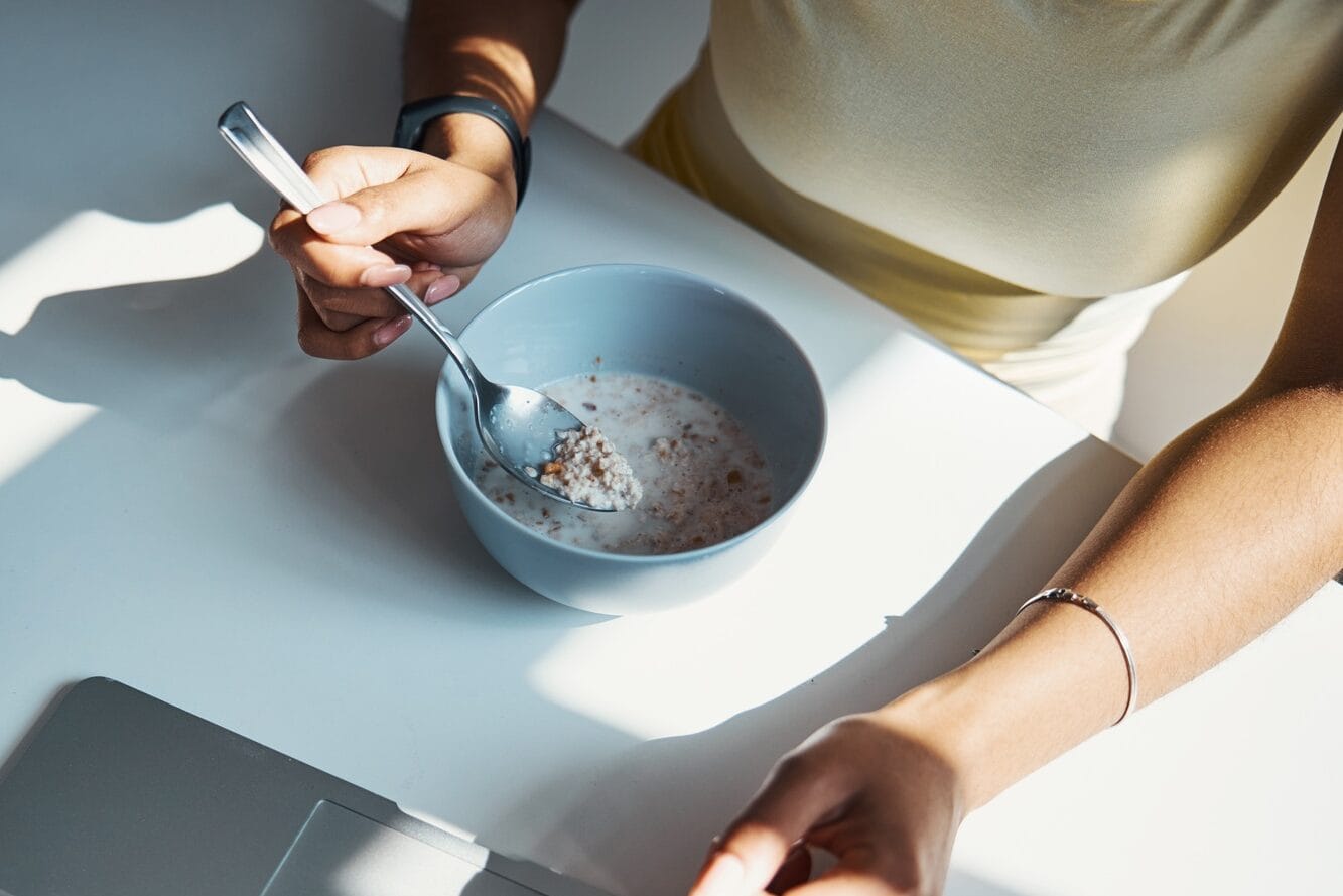 Young woman eating oatmeal and using notebook at home jajandikitid Young woman eating oatmeal and using notebook at home